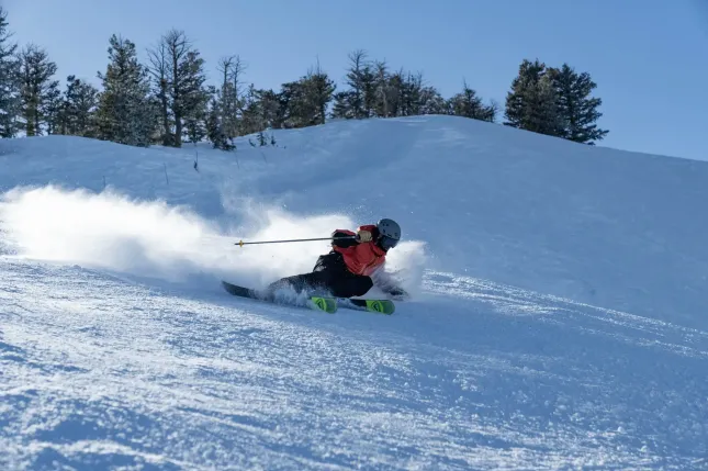 Ski coming down a slope with a snow in the background