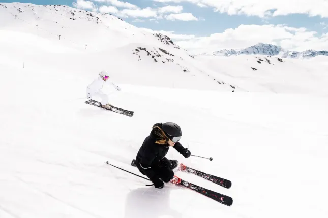 Ski coming down a slope with a snow in the background