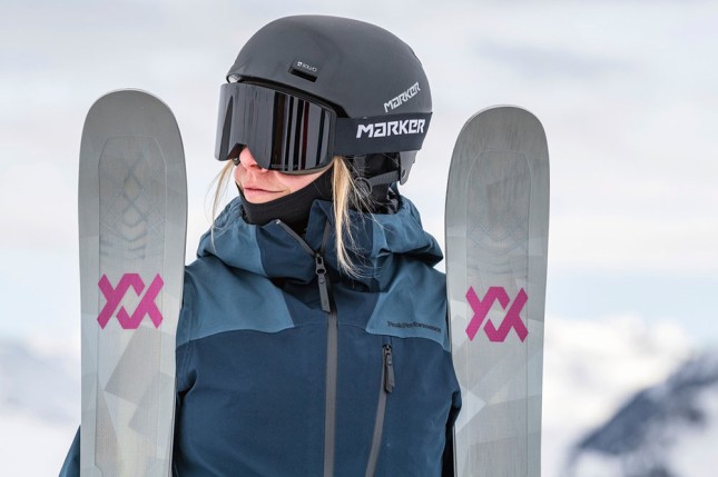 Female dressed ski clothing wearing helmet and goggles and holding skis