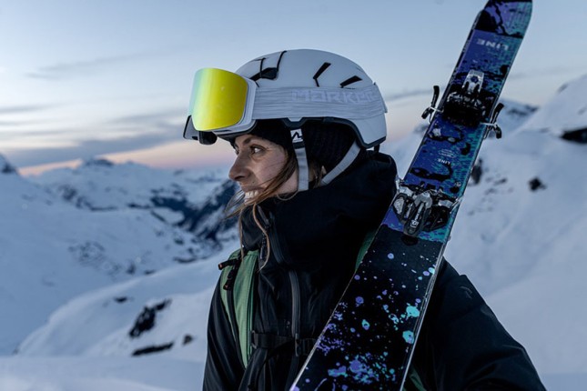 Female wearing Marker helmet and ski goggles while holding skis