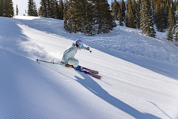 Skier skiing on treelined run from left to right