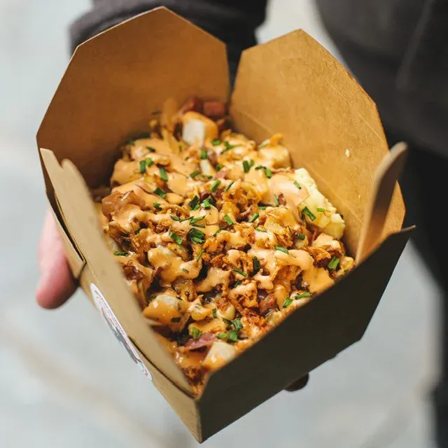 A hand holding a takeaway box of chips and poutine