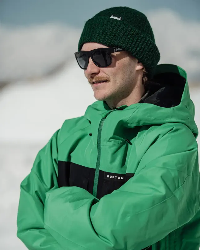 Man with a green coat with his arms crossed with a snowy background