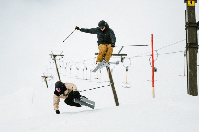 Two skiers skiing towards the camera close to a ski lift